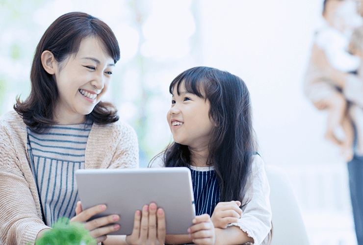 母親と娘がタブレットを持ちながら顔を見合わせている写真